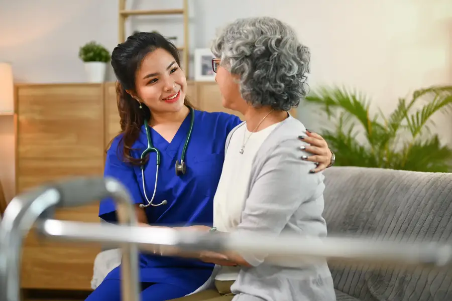 A nurse with a stethoscope shares a warm embrace with an older woman at home.